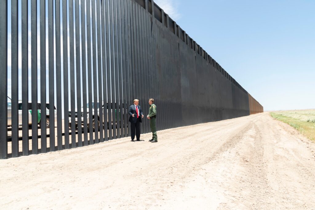 Donald Trump stands at the U.S.–Mexico steel border barrier while meeting with the Border Patrol Chief.