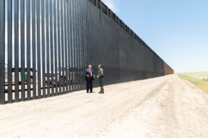 Donald Trump stands at the U.S.–Mexico steel border barrier while meeting with the Border Patrol Chief.