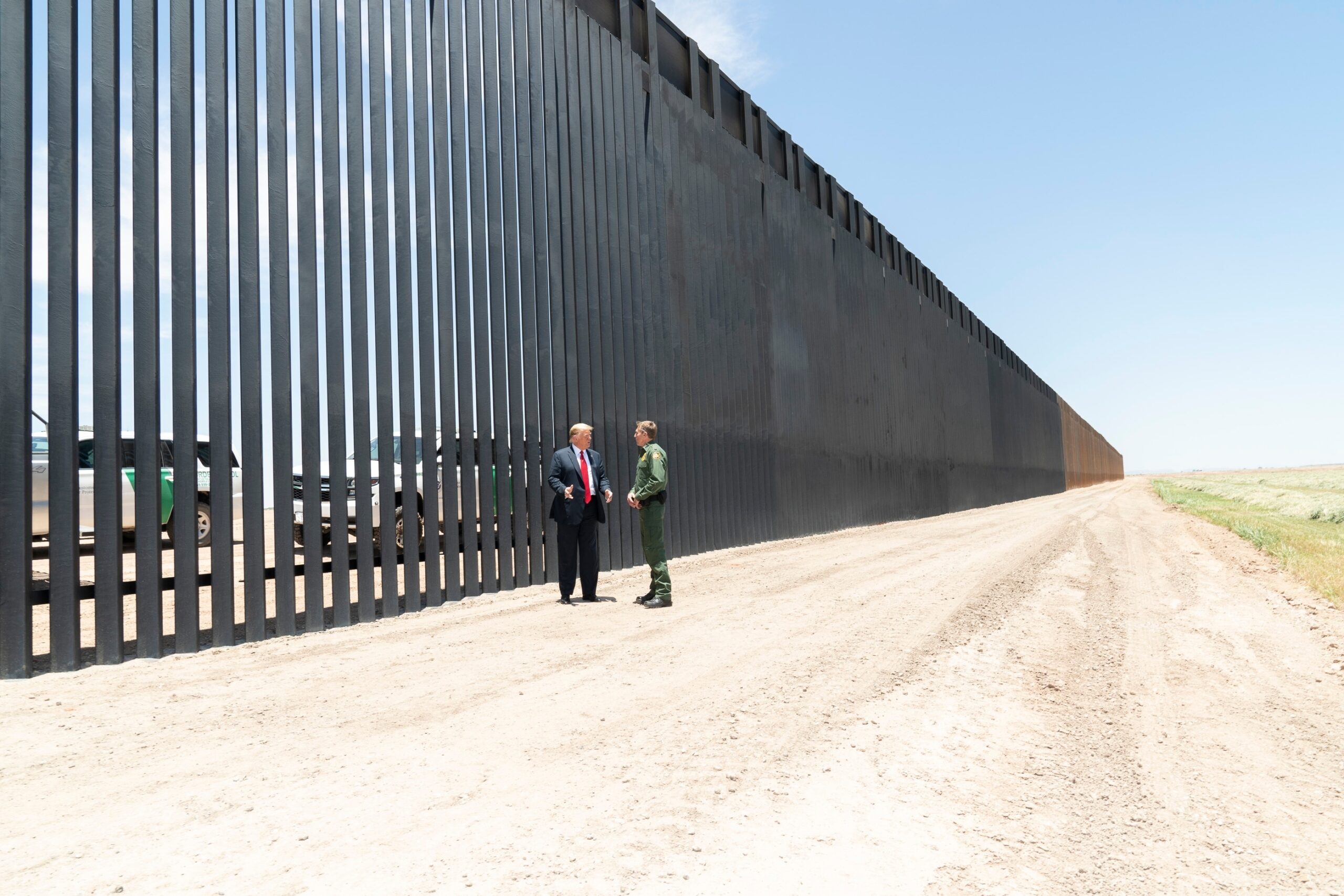 Donald Trump stands at the U.S.–Mexico steel border barrier while meeting with the Border Patrol Chief.